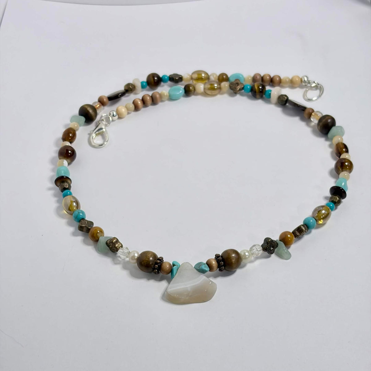 A beaded necklace with a central agate and turquoise stone, featuring brown, beige, and light blue beads, displayed on a white surface.