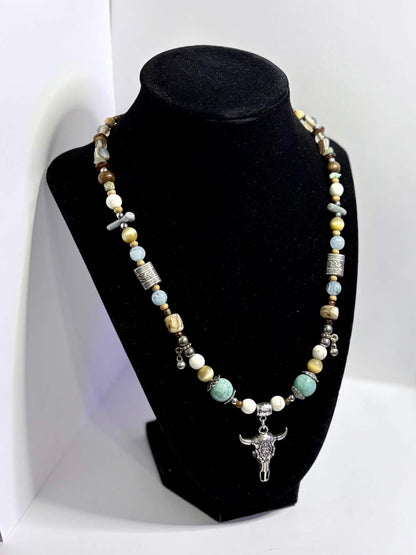A beaded necklace with a silver-toned floral steer pendant displayed on a black jewelry bust, set against a white backdrop.