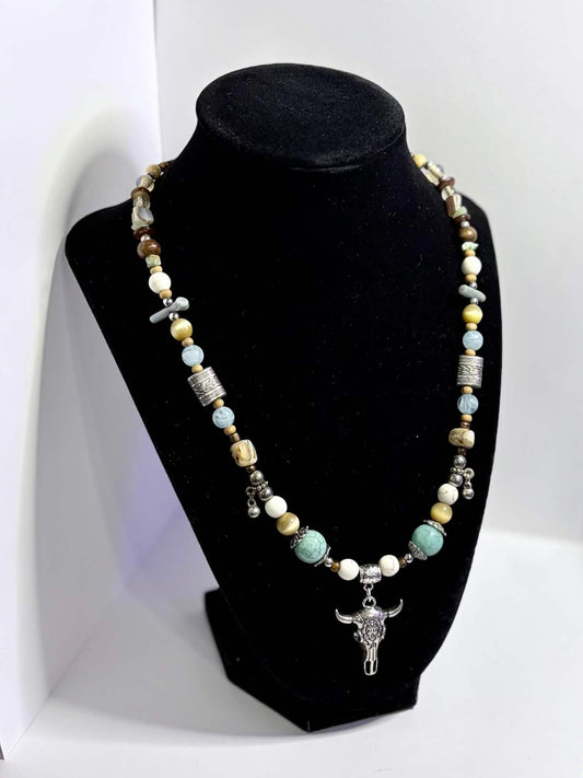 A beaded necklace with a silver-toned floral steer pendant displayed on a black jewelry bust, set against a white backdrop.