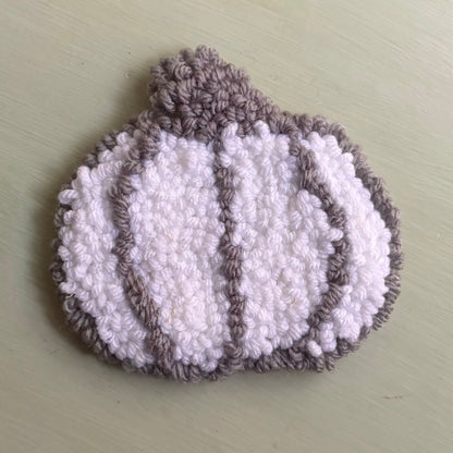 A punch needled coaster pumpkin-shaped white and gray, photographed on a table.
