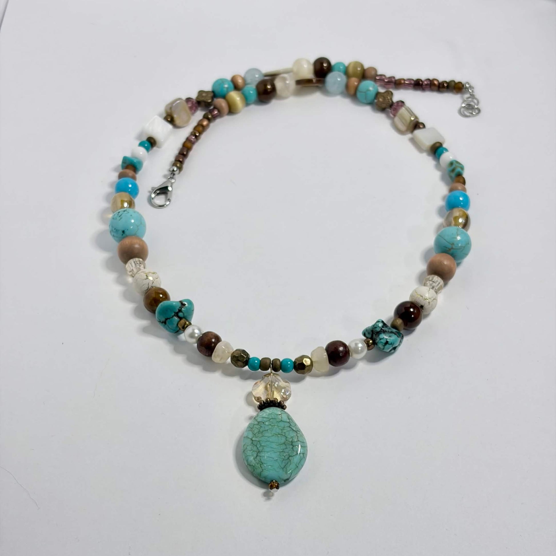 A beaded necklace with a large turquoise stone pendant, featuring a mix of turquoise, brown, cream, and white beads, displayed on a white background.