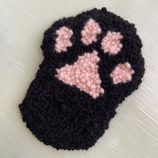 Black punch needle paw-shaped coaster with pink center on a light background