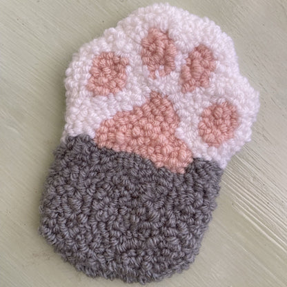 Punch needle paw coaster on a light green background