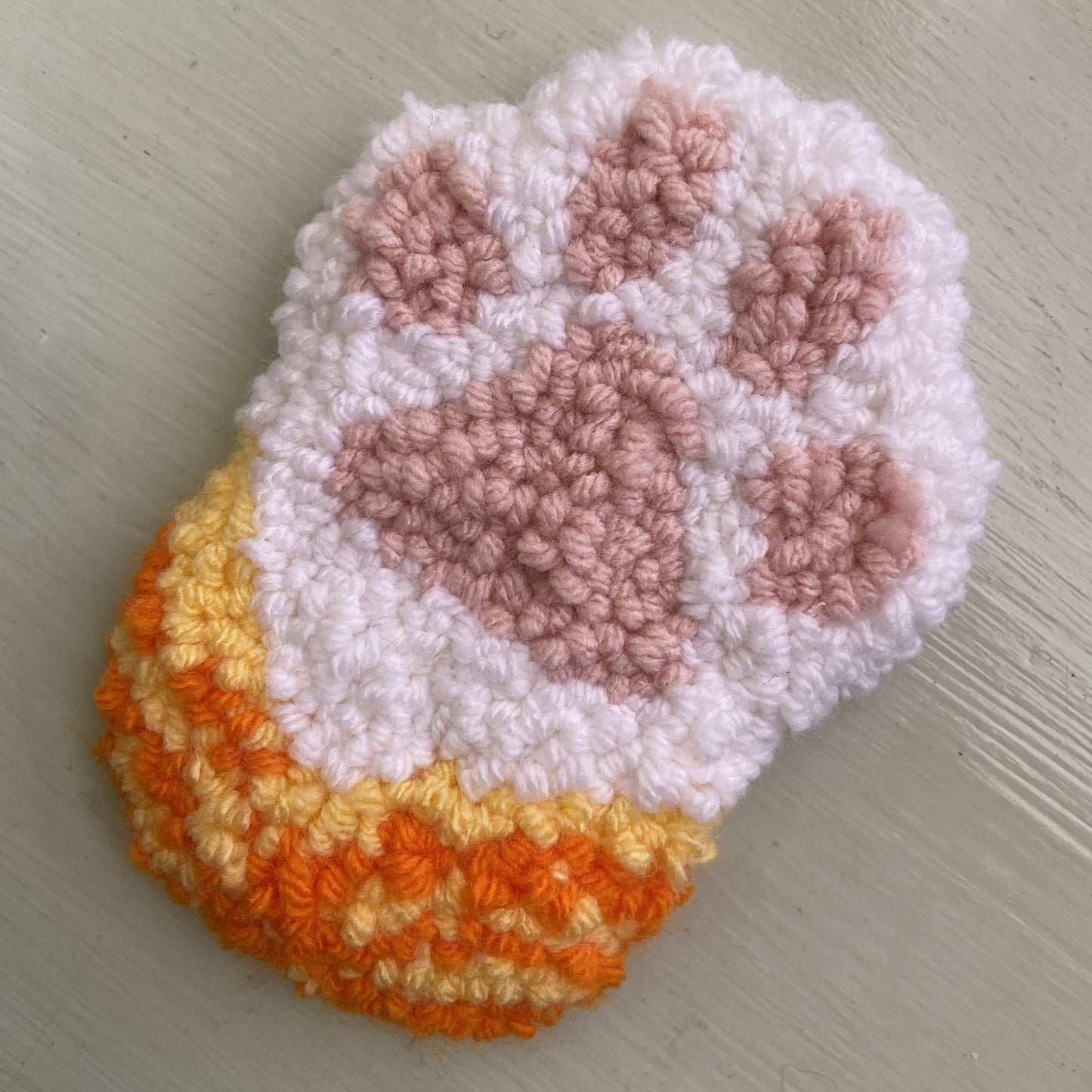 Punch needle paw print with orange, white, and pink colors on a light background